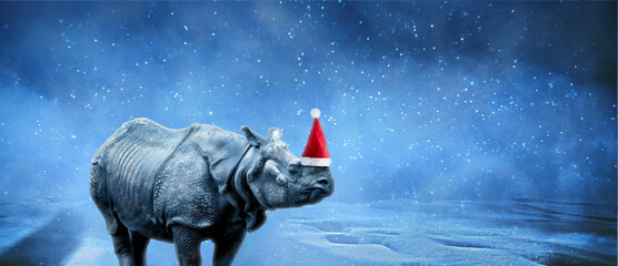 rhinoceros in Santa Claus hat over snowy background, merry christmas concept, panoramic image © alesmunt