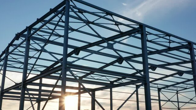 Metal construction - steel frame silhouette of unfinished industrial hall. Structure (framework) consisting of iron girders and beams meant to support the roof with sun shining through the grid.