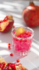 Summer cocktail with pomegranate and ice. White table with sunlight and palm leaf shadow. Summer, tropical and juicy concept