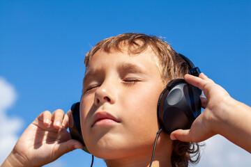 Boy listens to music on headphones on background of blue sky