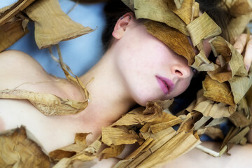 beautiful sensual seductive portrait of a young brunette woman, lying between leaves of dry...