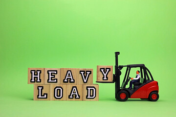 heavy load written on wooden blocks with the letter Y being added by a scale model forklift truck.