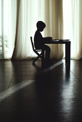 The silhouette of a child at home at a desk doing homework, drawing or writing.