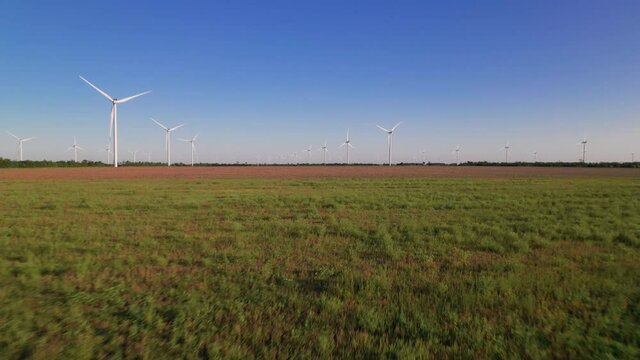 Windmills in a green field. Wind farm with turbine cables for wind energy. Renewable energy source, earth care. Drone video of wind power station, 4k. Botiyevska Ves, Ukraine.