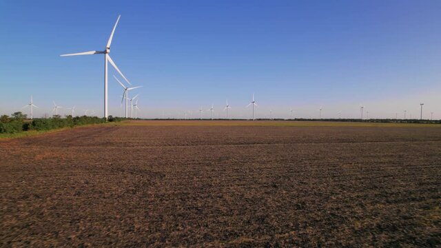 Windmills in a plowed field. Wind farm with turbine cables for wind energy. Renewable energy source, earth care. Drone video of wind power station, 4k. Botiyevska Ves, Ukraine.