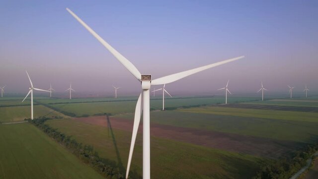 Windmills with rotating wings among green fields. Wind farm with turbine cables for wind energy. Renewable energy source, earth care. Drone video of wind power station, 4k. Botiyevska Ves, Ukraine.