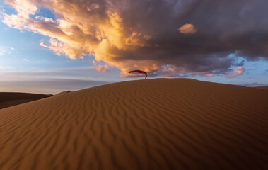 Girl walking on the sand dunes in the distance holding a red cloth