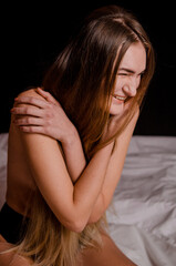 Naklejka premium Beautiful young woman with blonde hair in black underwear is sitting on bed in aesthetic poses, on a black background
