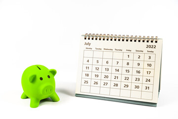 July 2022 calendar and green piggy bank on white background