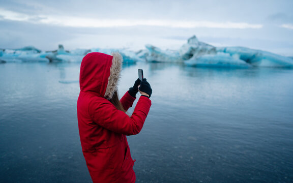 Girl taking a picture of a blue iceberg in ice lagoon at Iceland.  Woman taking photograph of beautiful Icelandic nature with Vatnajokull.
