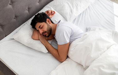 Asleep young arab man sleeping, resting peacefully in comfortable bed, lying with closed eyes, free space