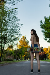 Woman standing on her back, holding her skateboard with both hands, looking to the side. On a city street