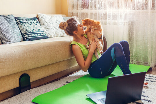 Home workout during coronavirus covid lockdown. Woman relaxing after training online using laptop playing with cat.