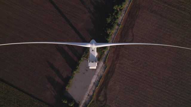 Windmill with huge rotating blades, top view. Wind farm with turbine cables and wings for wind energy. Renewable energy source. Drone video of wind power station, view from the top, 4k.