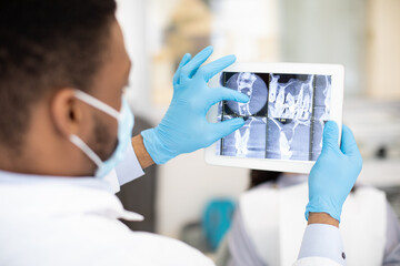 African American Male Dentist Doctor Using Digital Tablet, Checking Patient's Teeth Xray