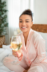 Time for youself concept. Portrait of happy african american lady sitting on bed, drinking wine and...