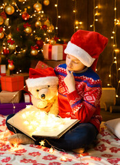 Child girl reading a book in new year or christmas decoration. Holiday lights and gifts, Christmas...