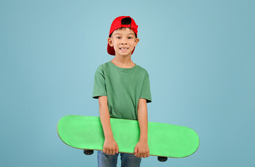 Little asian boy in red hat holding skateboard and looking at camera © Prostock-studio