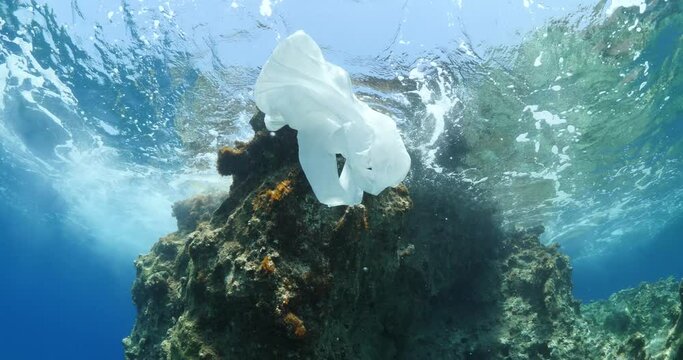 plastic bag underwater bad for fish with sun rays water waves hit to rocks background ocean pollution