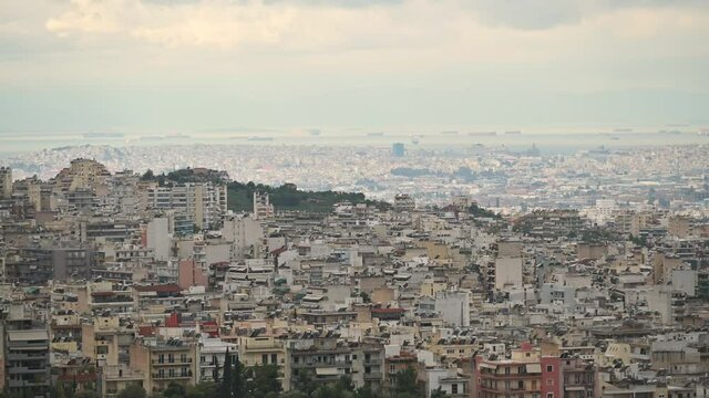 Time lapse video shows north suburbs of Athens city on a cloudy day. Sea with ships moving at the background.