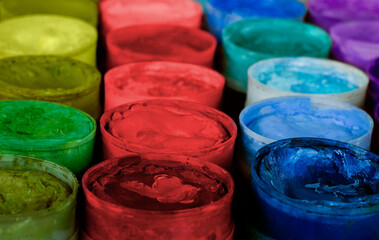 Row of paint pots in a variety of colors, most of which are primary. The pots have seen lots of...