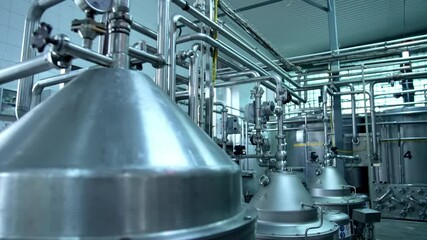 Big cisterns for storing and fermenting milk at diary factory. Stainless steel pipes crossing and connecting reservoirs with each other. Close up.