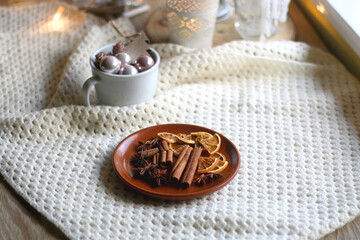 Plate with cinnamon, anise and dry oranges, cozy blanket, various Christmas deocrations and lit candles. Hygge at home. Selective focus.