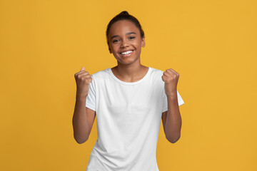 Happy teenager african american girl student in white t-shirt rejoices to win and success,...