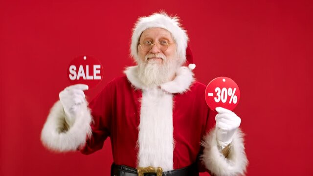 Christmas SALE -30 Off. Cheerful Santa Claus is Dancing and Joyful From Christmas Sale Holding Two Banners With Inscription SALE and -30 Off Showing Off Inscriptions to Camera on Red Background.