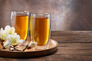 Two glass cups of tea and flowers on wooden table