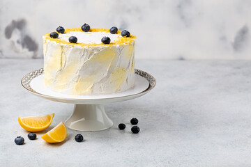 Lemon cake decoraed fresh blueberries on cake stand, white table.