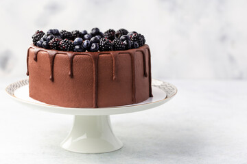 chocolate cake with cream, berries and dripping chocolate on cake stand, on white background