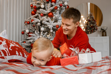 Photo of funny cheerful father tickle his laughing little son wearing red sweaters in decorated...