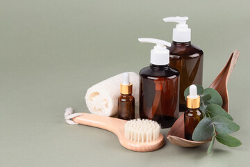 Set of natural bathroom amenities - glass dropper bottles with natural organic cosmetics, natural face or body dry brush, eucalyptus oil, cream, lotion, essential oils on green background. Mockup