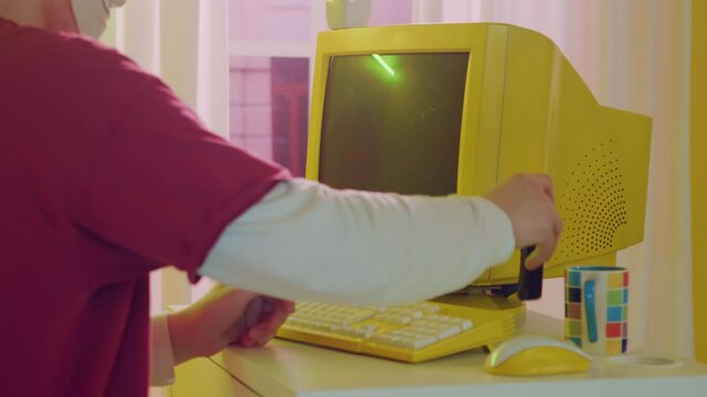 Man hacker in mask is using retro technologies personal computer, typing on yellow keyboard, using old mobile phone to make a call, large yellow monitor is standing on table, Close up, Slow motion.