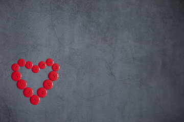 Heart is composed of red buttons on a dark gray background. Accessories for needlework. Concept Valentines Day.