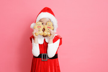 smiling young girl holding ginger bread men stand in front of pink background