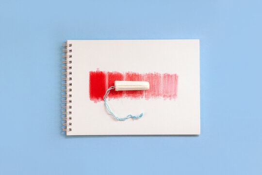 Notebook with red rectangles and feminine hygiene tampon. Concept intensity of menstrual flow. Top view