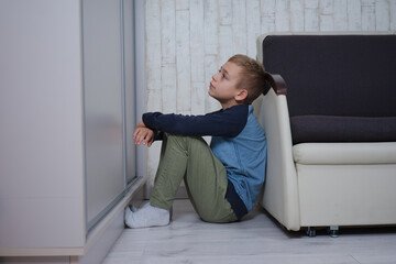 mały chłopak siedzi oparty o fotel, jest smutny - obrazy, fototapety, plakaty
