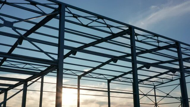 Metal construction - steel frame silhouette of unfinished industrial hall. Structure (framework) consisting of iron girders and beams meant to support the roof with sun shining through the grid.