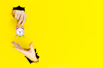 Ringing twin bell vintage classic pink alarm clock in female hand isolated in torn hole of yellow background. Rest hours time of life good morning night wake up awake concept. Mockup, copy space.