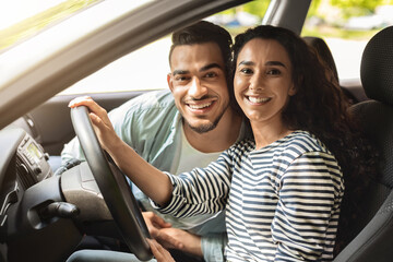 Beautiful young woman driver posing inside new car with boyfriend