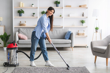 Cheerful lady cleaning rug carpet with vacuum cleaner