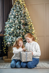 Obraz na płótnie Canvas Two little sisters open gift boxes under the tree in the room. Winter holidays concept, merry christmas and family