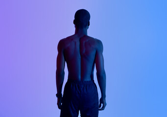 Back view of strong young black man with naked torso posing in neon light