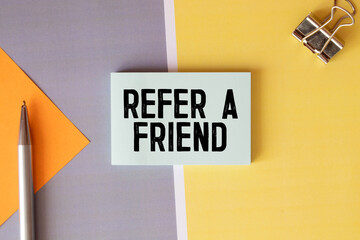 Text Refer a friend written on the white paper with pen and a cup of coffee aside.