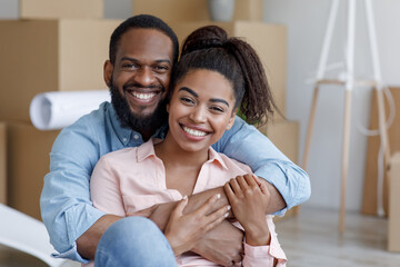 Satisfied young african american wife and husband hugging in new apartment with boxes