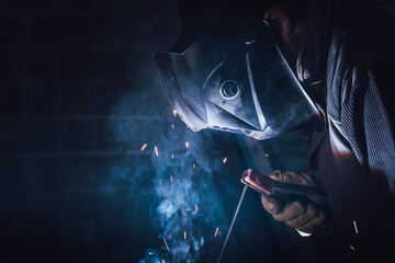 Welder working in a factory welding with an electrode