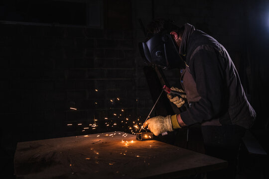 Welder using an electrode to weld a metal plate with yellow sparks