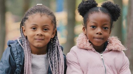 Portrait preteen cute children close-up two sisters spend time in city park little friends looking at camera happily smiling small girls sitting on bench outdoors careless childhood cheerful vacations